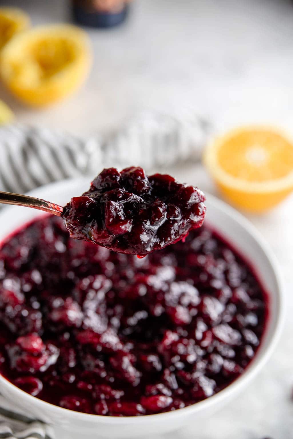An easy red wine cranberry sauce in a bowl with a spoonful of red sauce and orange segments. 