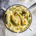 A bowl of roasted garlic mashed potatoes with brown butter and fresh sage leaves.