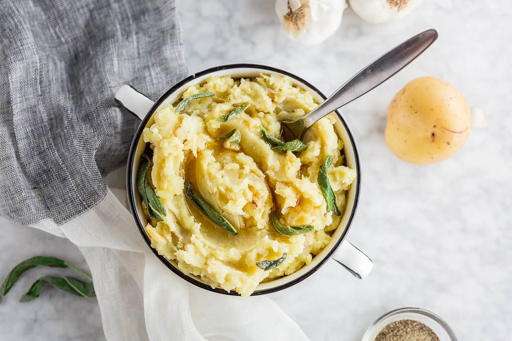 A bowl of gluten-free brown butter roasted garlic mashed potatoes with sage wth a spoon.