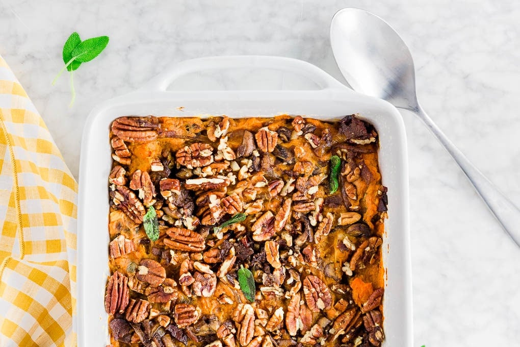 A baking dish with easy savory sweet potato casserole that is both gluten-free and dairy-free, topped with bacon, caramelized onions, mushrooms, sage and pecans.