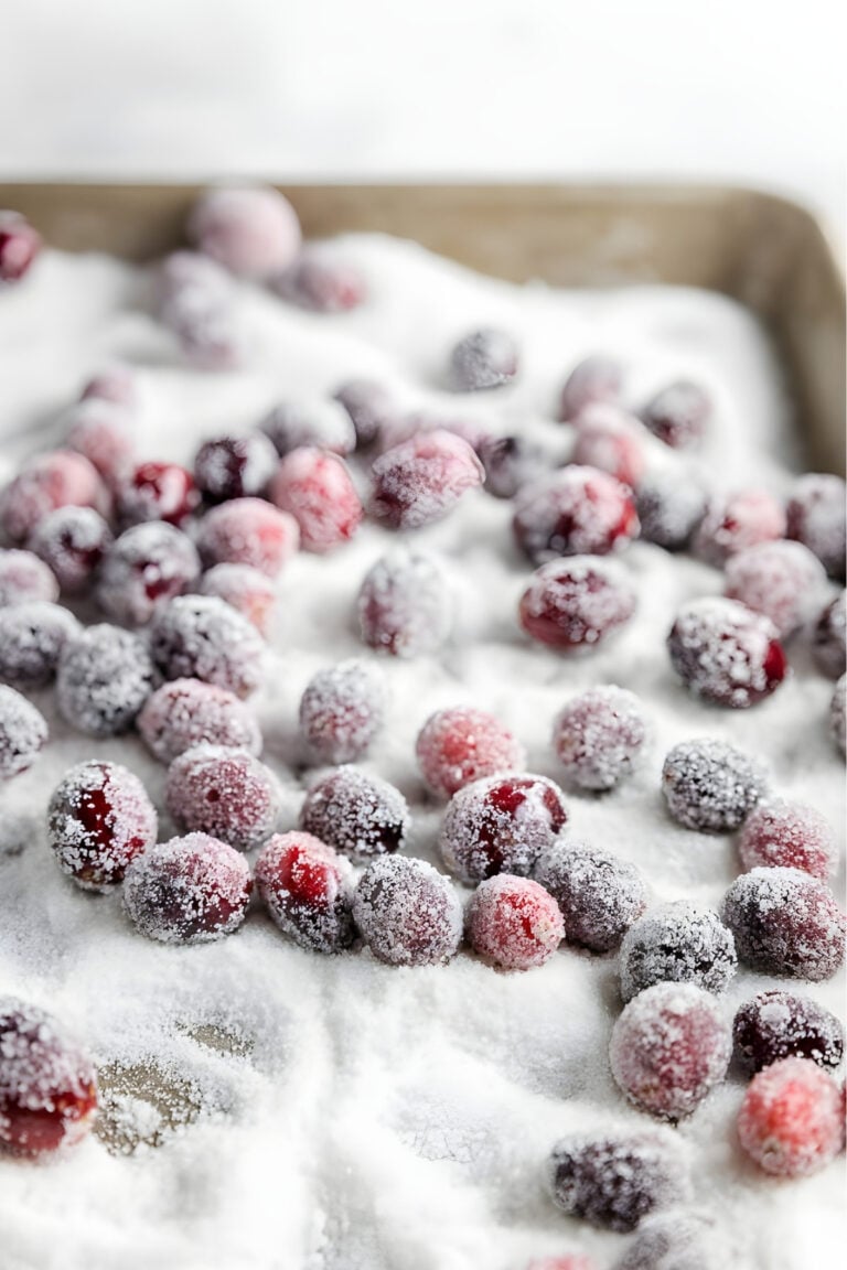 Sugared cranberries on a sheet pan with a layer of granulated sugar under them.