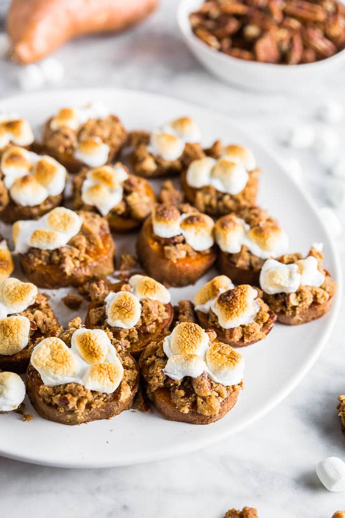 A plate with sweet potato casserole bites with a gluten-free brown sugar pecan crumble and toasted marshmallows with a bowl of pecans. 