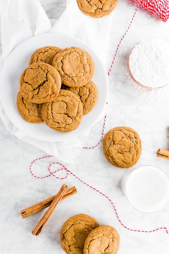 A plate of easy chewy ginger molasses cookies with cinnamon sticks and a glass of almond milk. 