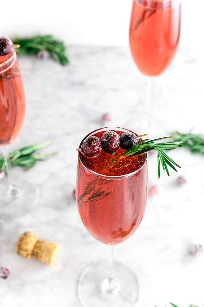 three champagne flutes filled with cranberry juice and prosecco with sugared cranberries and fresh rosemary in a festive cranberry mimosa cocktail