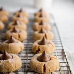 rows of peanut butter blossoms with a chocolate kiss on top on a cooling rack with a glass of milk.