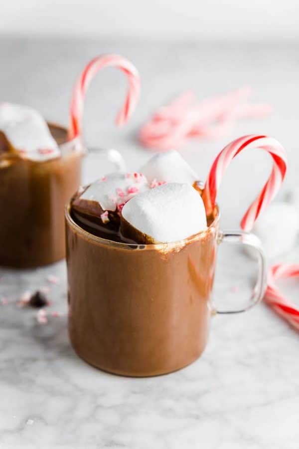 Mug of peppermint hot cocoa with marshamllows and peppermint candy canes with chocolate chips.