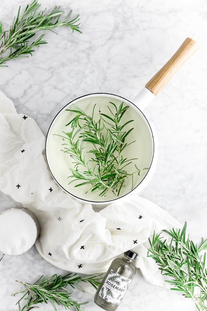 a pot of rosemary simple syrup steeping with a bottle of rosemary infused simple syrup, fresh rosemary sprigs and a cup of sugar. 