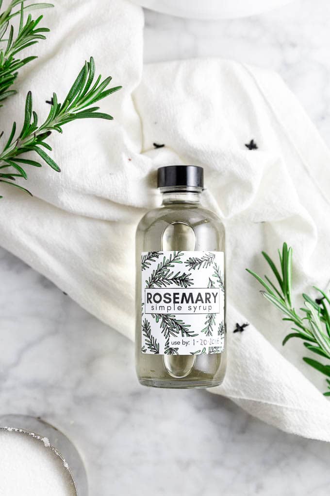 a bottle of rosemary simple syrup with fresh rosemary sprigs and sugar