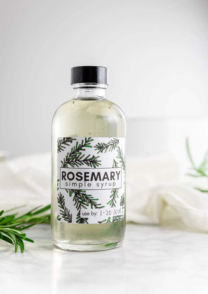 a bottle of rosemary simple syrup with a free printable label with sprigs of fresh rosemary. 