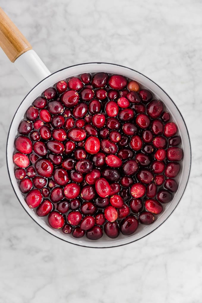 A saucepan filled with simple syrup and fresh cranberries soaking ready to be rolled in sugar for sparkling sugared cranberries. 