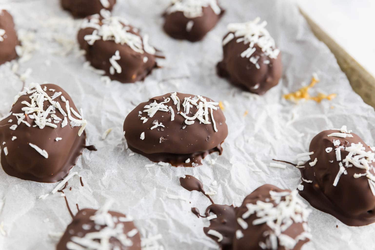 Chocolate and coconut covered dates stuffed with peanut butter on a sheet pan with parchment paper. 