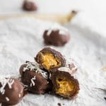 Several chocolate covered peanut butter stuffed dates topped with shredded coconut on white parchment paper.