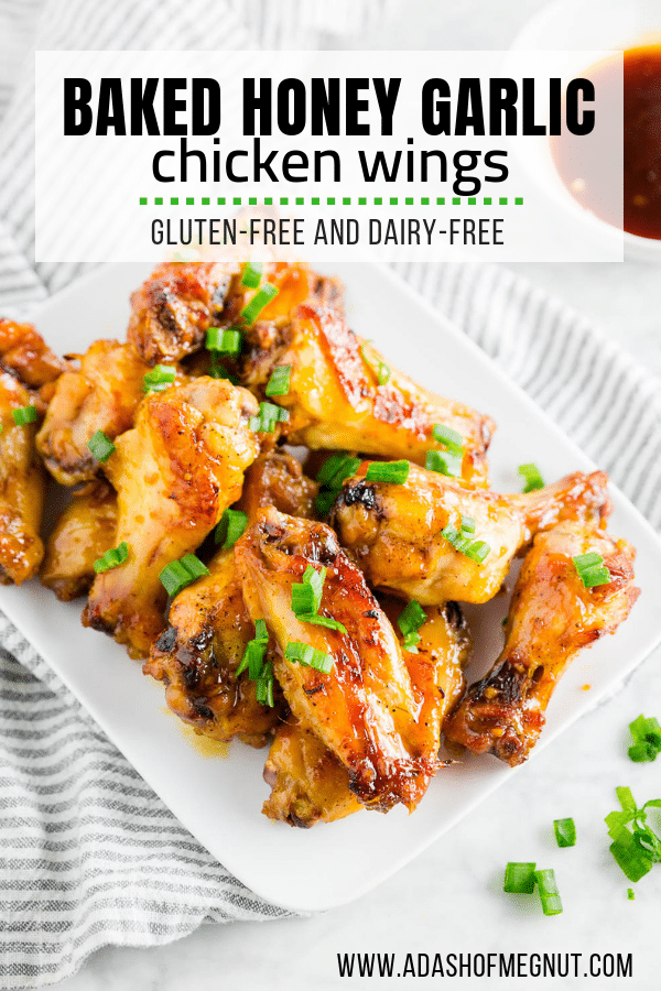 A plate of baked honey garlic chicken wings topped with green onions on a white table with a side of honey garlic sauce.