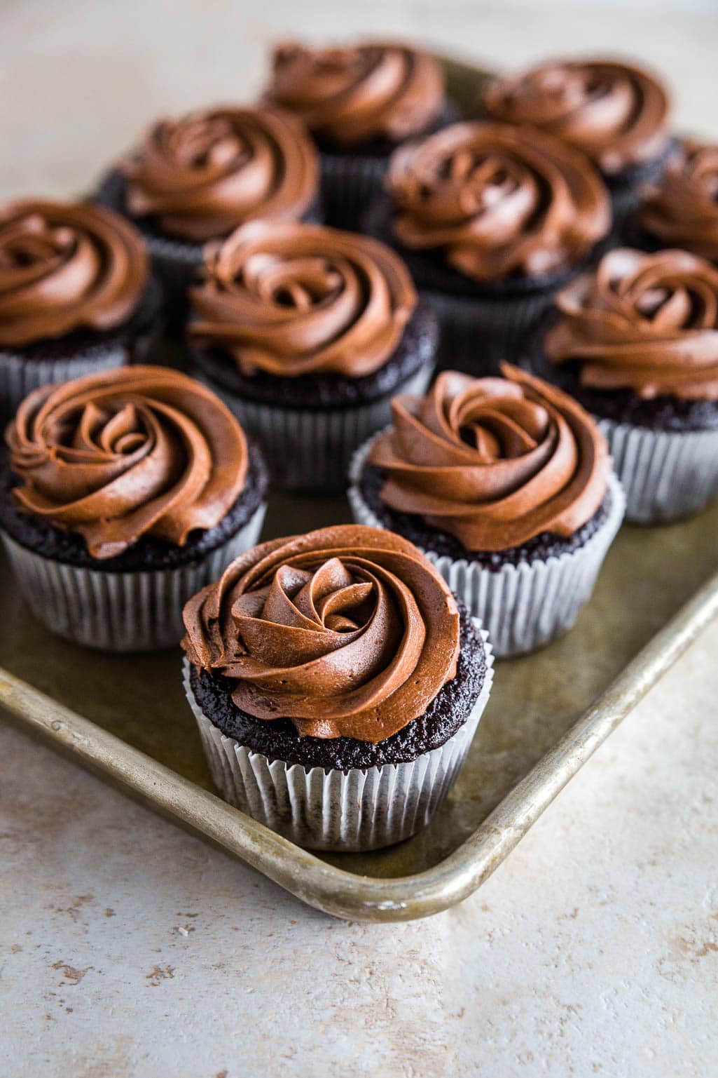 Photo of a sheet pan filled with a dozen gluten-free chocolate cupcakes with chocolate buttercream frosting. 