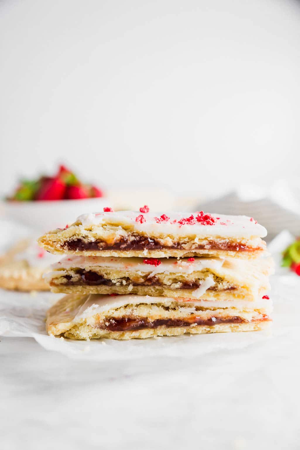 A stack of three gluten-free strawberry pop tarts with a bowl of fresh strawberries. 