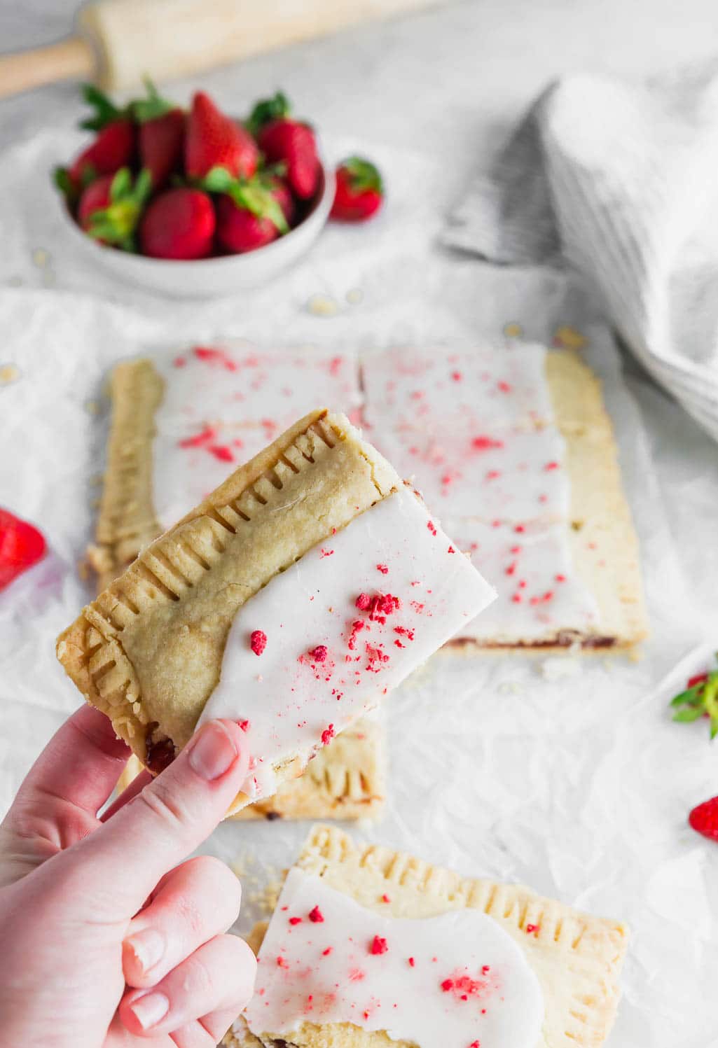 A photo of a piece of a giant strawberry pop tart in a hand. 