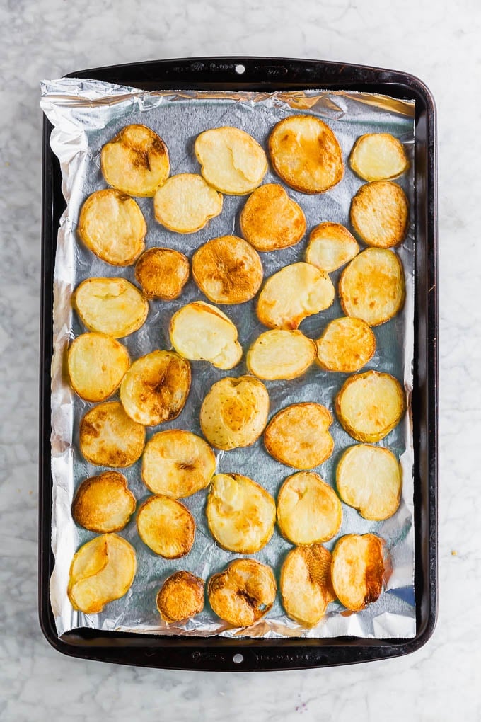 A photo of a baking sheet lined with aluminum foil with slices of potatoes that have been roasted in the oven. 