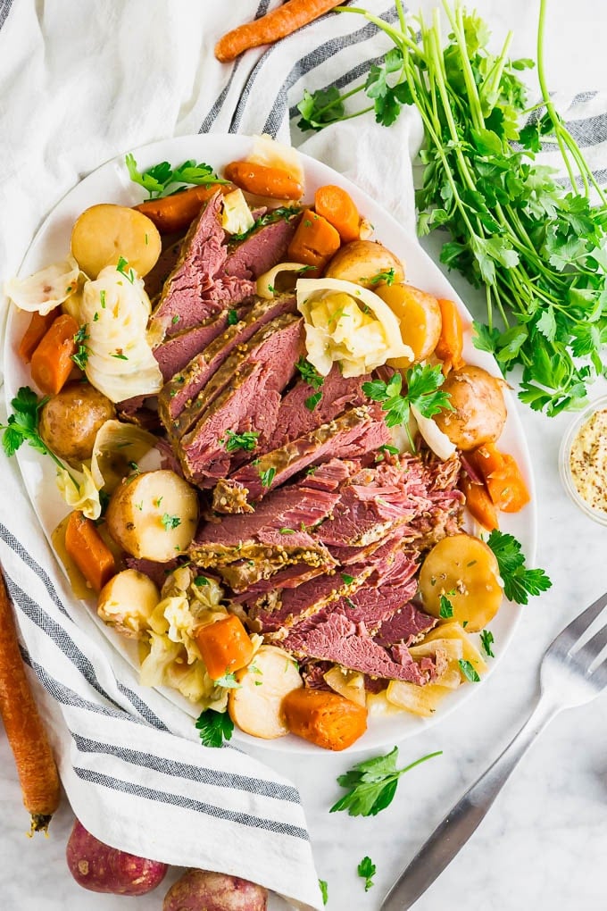 A platter of crock pot corned beef with red potatoes, carrots, cabbage, onion and fresh parsley.