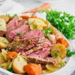 A photo of a platter of corned beef with potatoes, carrots, parsley, cabbage and onions.