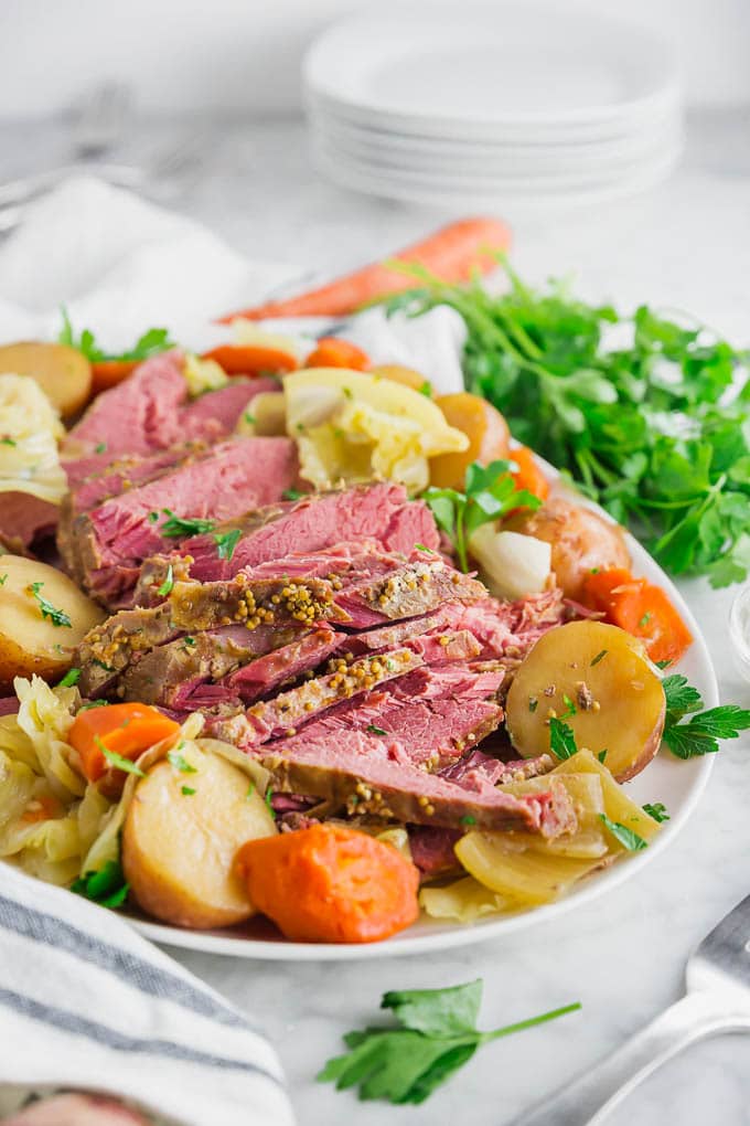 A photo of a platter of corned beef with potatoes, carrots, parsley, cabbage and onions. 