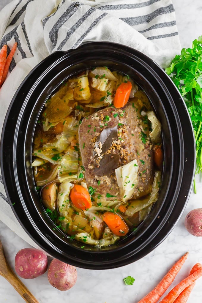 A photo of a crock pot with corned beef, carrots, onion, cabbage and potatoes. 