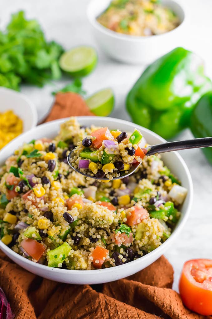 A bowl of southwest quinoa salad with corn, tomato, black beans, onion, cilantro and avocado with a spoon. 