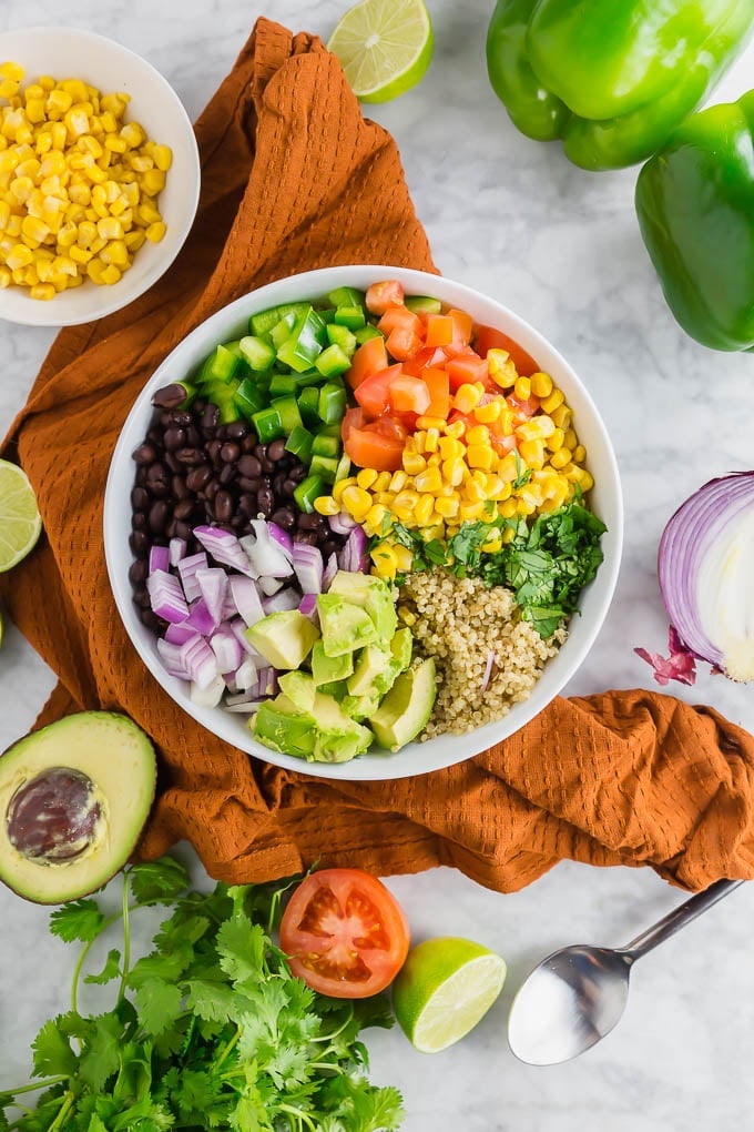 A bowl filled with quinoa, black beans, bell pepper, tomato, corn, cilantro, avocado and red onion. 