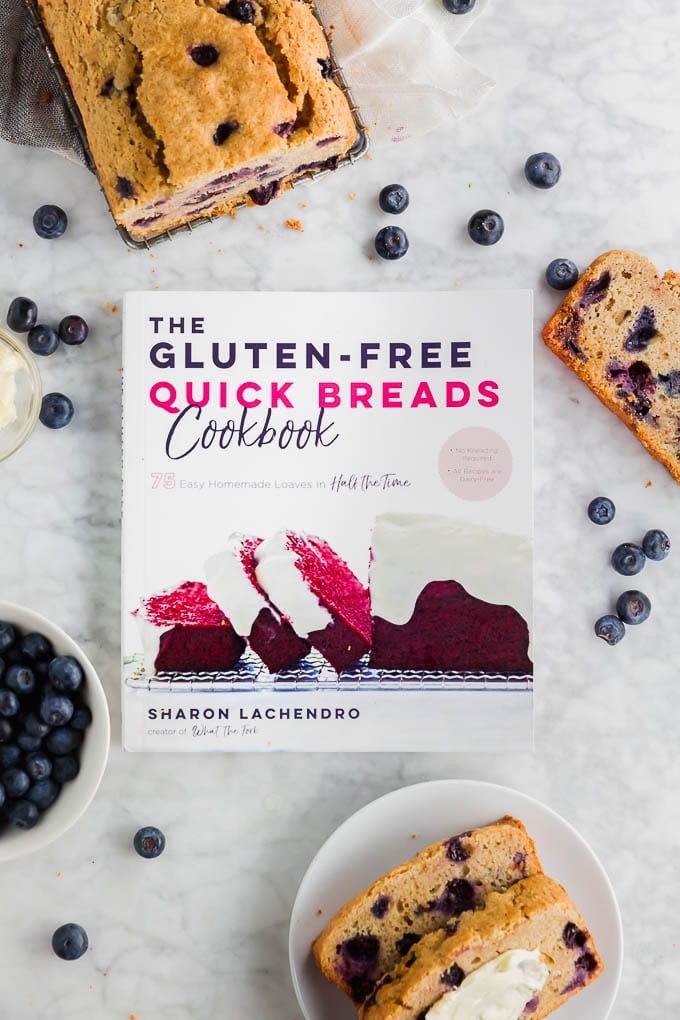 A photo of The Gluten Free Quick Breads Cookbook written by Sharon Lachendro with a loaf of blueberry muffin bread and fresh blueberries. 