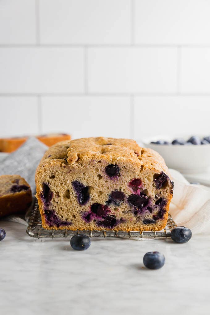 A loaf of gluten free blueberry muffin bread on a table with fresh blueberries. 