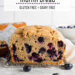 A loaf of gluten free blueberry muffin quick bread on a table with fresh blueberries.