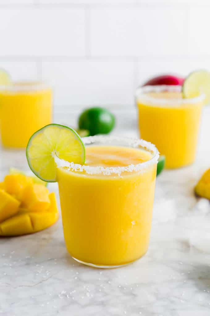 A photo of three glasses of frozen mango margaritas with lime wedges and a salted rim.