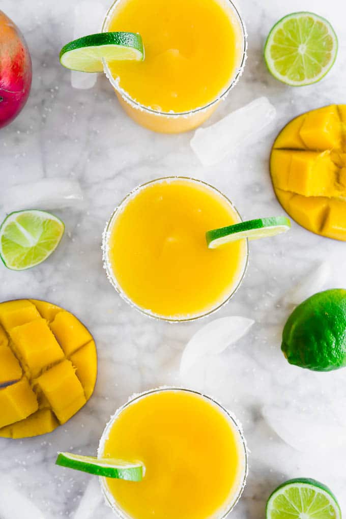 A photo of three glasses of frozen mango margaritas in a row with lime wedges and a salted rim on the glass. 