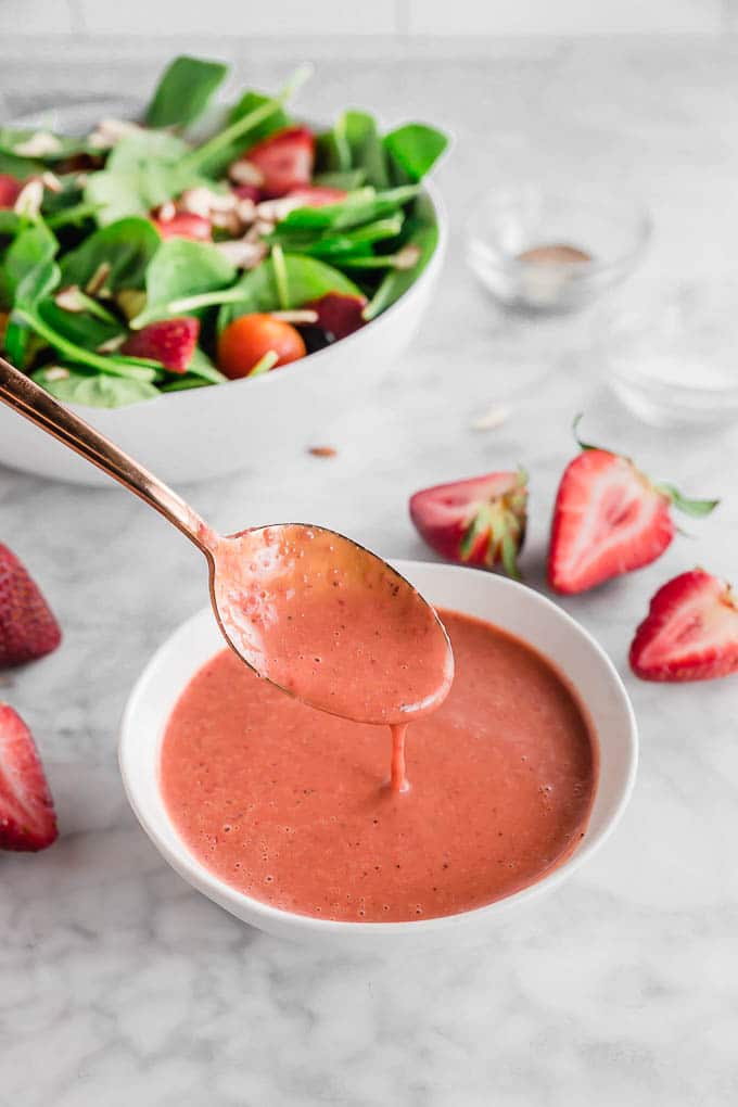 A photo of strawberry balsamic dressing in a bowl with a spoon drizzling some of the dresses. 