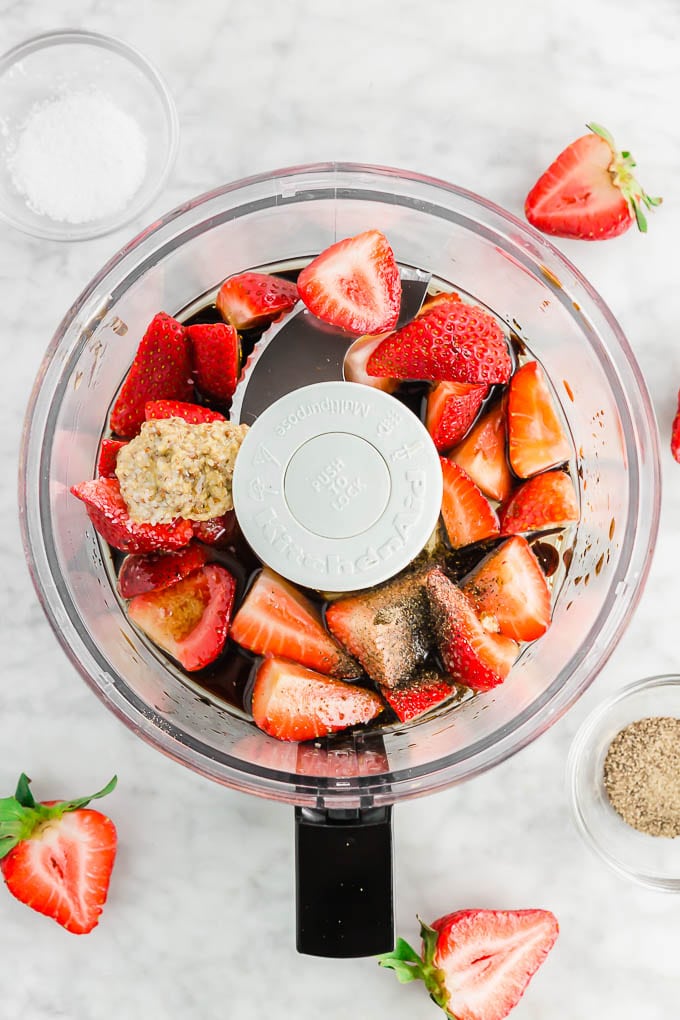 A photo of a food processor filled with strawberries, balsamic vinegar, olive oil, honey, salt, pepper and mustard to make strawberry vinaigrette. 