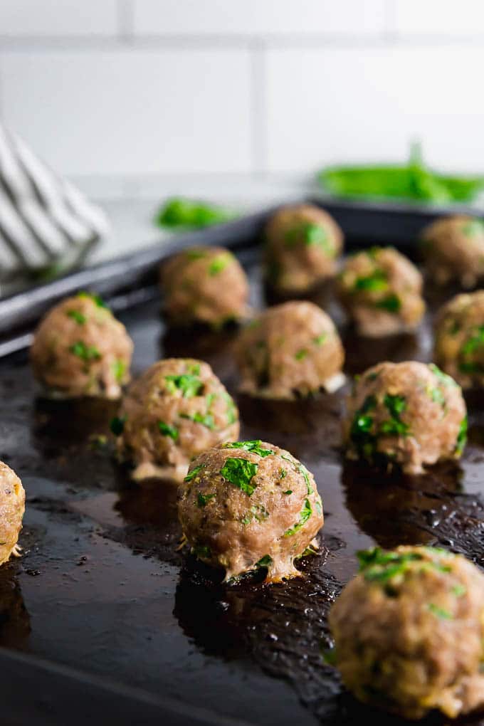 A sheet pan with baked turkey spinach meatballs straight from the oven with fresh spinach in the background. 