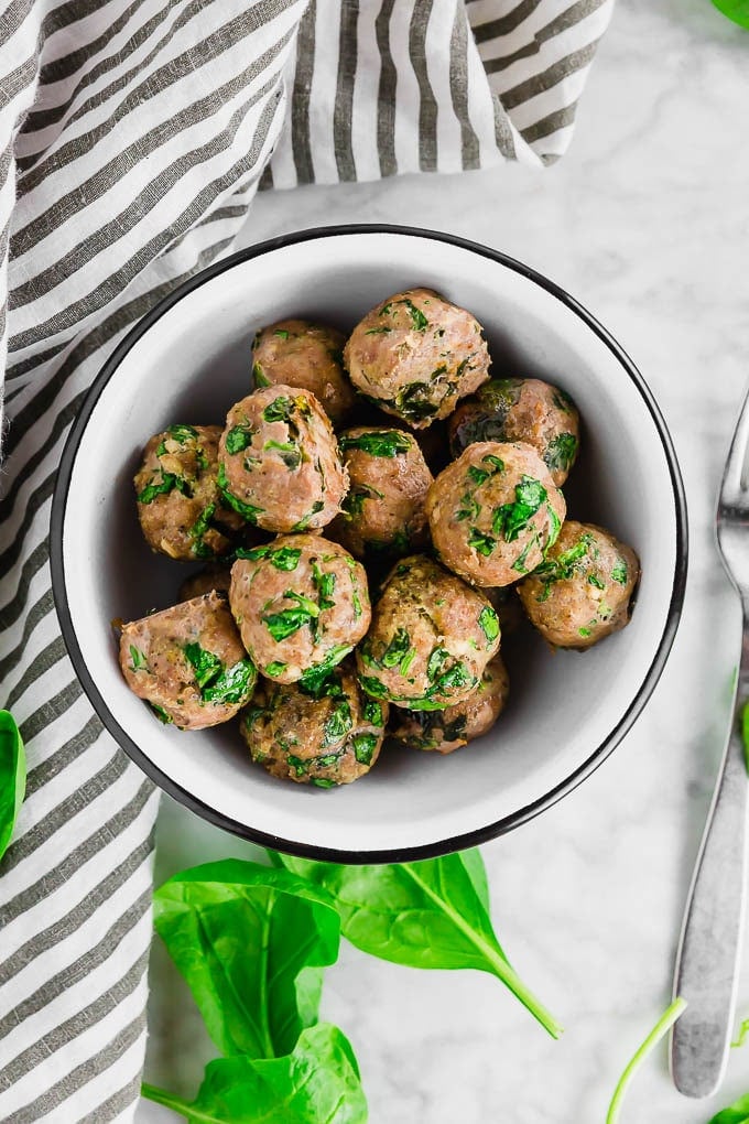 An overhead photo of a bowl of gluten free baked turkey meatballs filled with fresh spinach. 