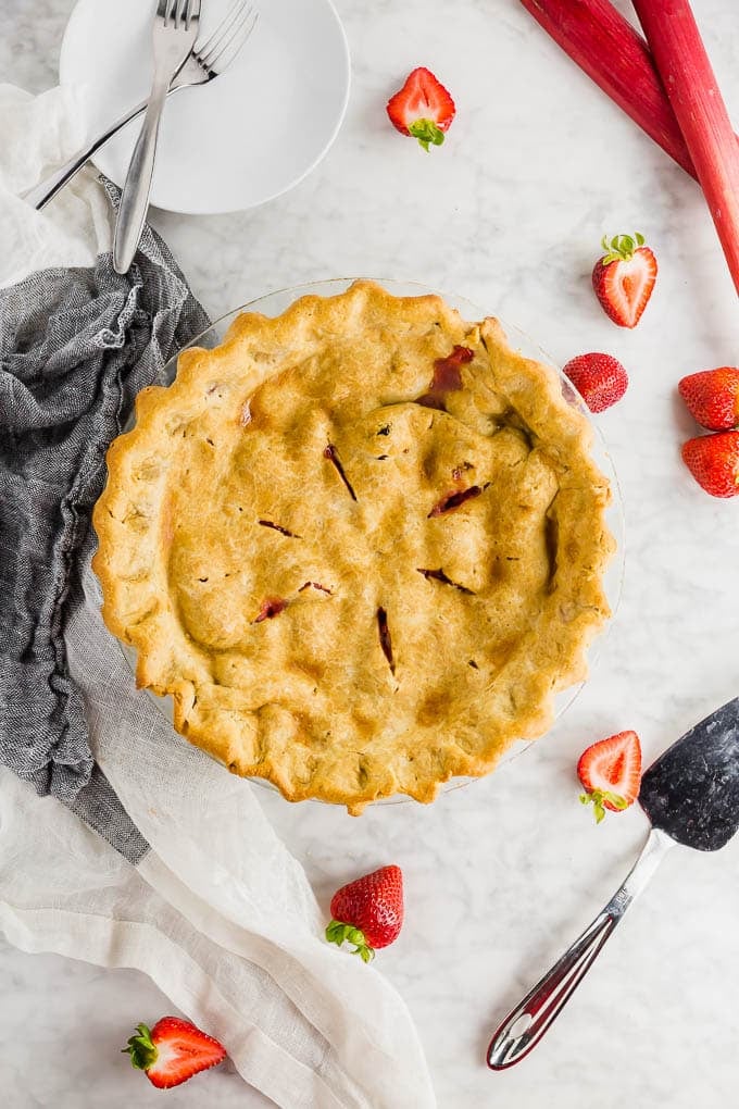 An overhead view of a strawberry rhubarb pie with a top crust and fresh strawberries and rhubarb on the side.