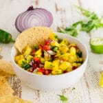 A bowl of homemade mango salsa with bell peppers, cilantro, and jalapeño in a bowl with a tortilla chip.