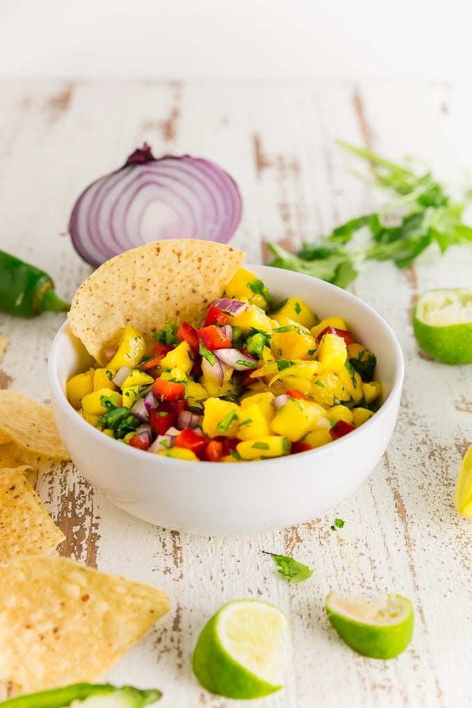 A bowl of homemade mango salsa with bell peppers, cilantro, and jalapeño in a bowl with a tortilla chip.
