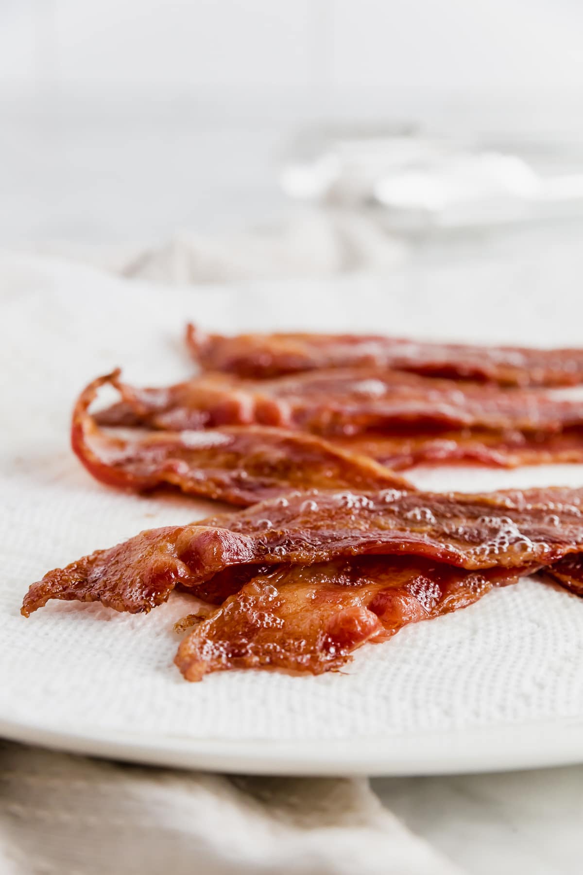 A plate covered with a paper towel and bacon straight fro the oven. 