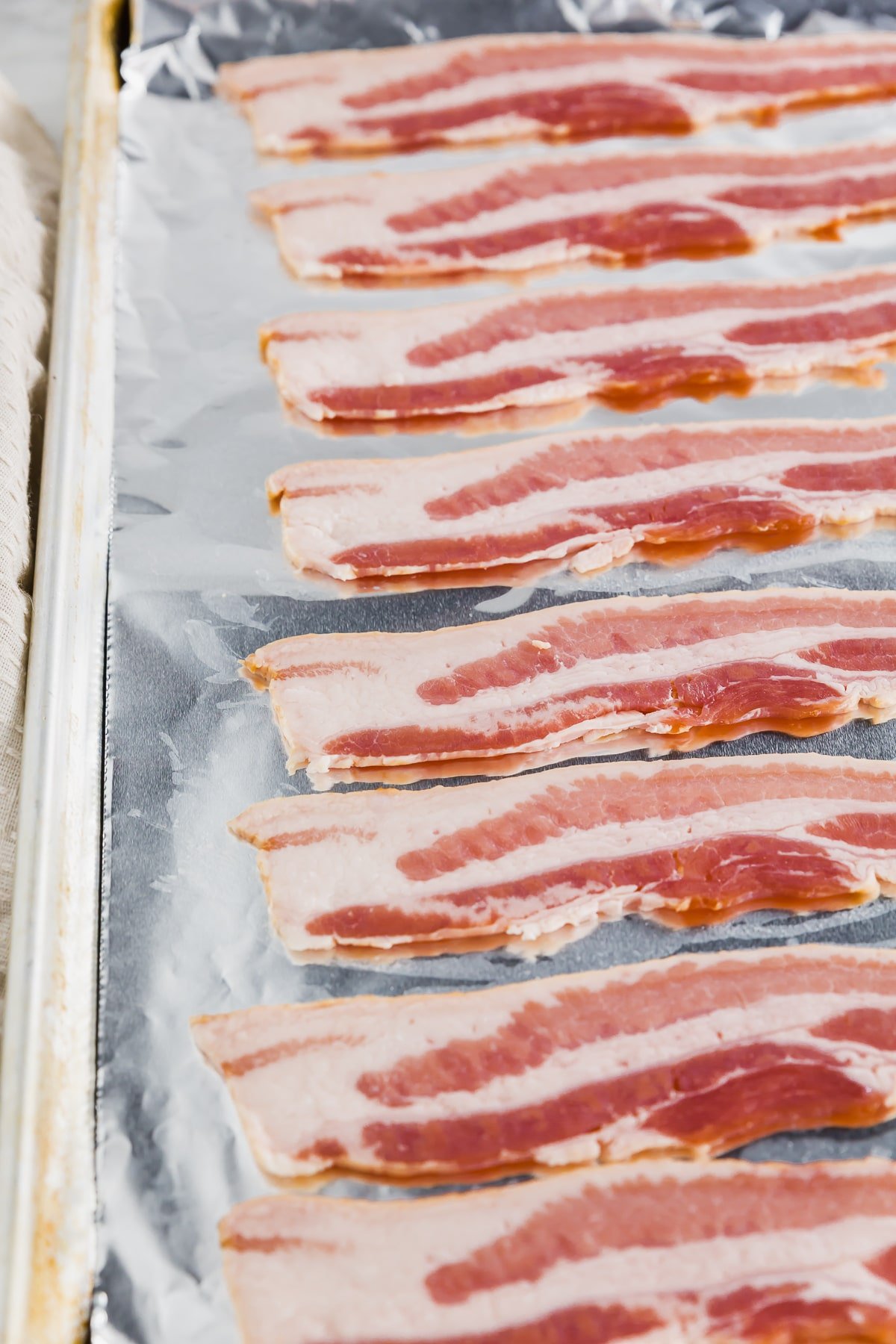 A baking sheet covered with aluminum foil and topped with bacon ready to be baked in the oven.