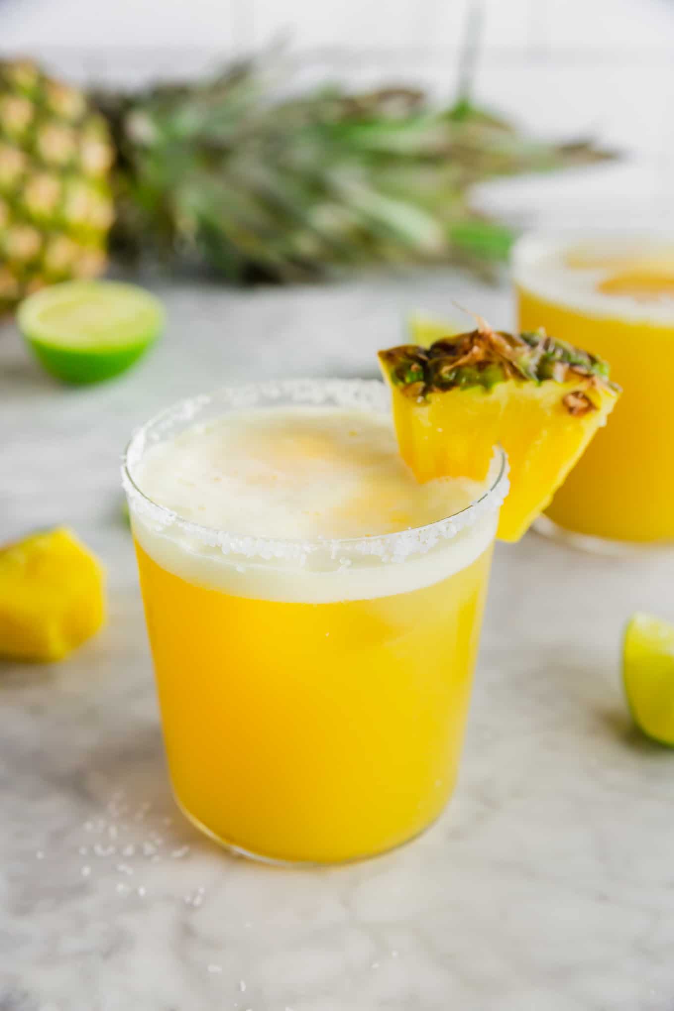 A photo of a glass filled with pineapple margarita with a wedge of fresh pineapple and lime.