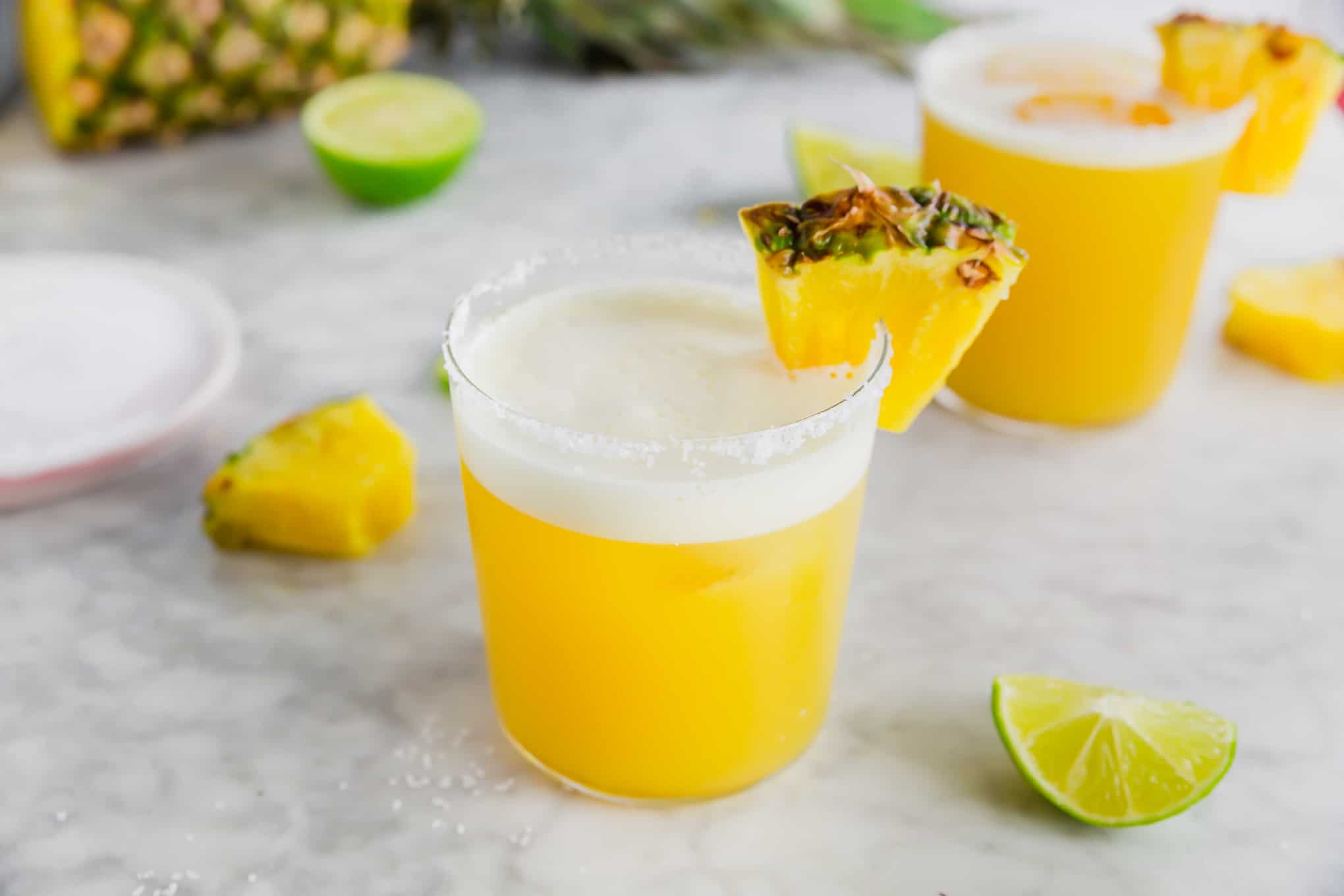 A photo of a pineapple margarita with a pineapple wedge and rim with kosher salt. 