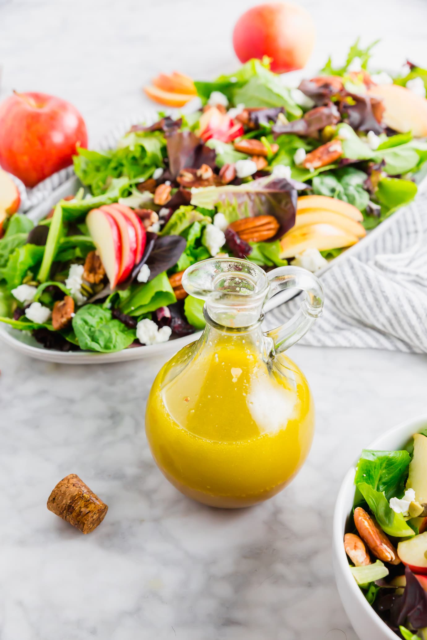 A bottle of homemade apple cider salad dressing in front of a spinach and apple harvest salad.