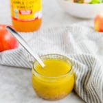 A photo of a jar of homemade apple vinaigrette with salad in the background.
