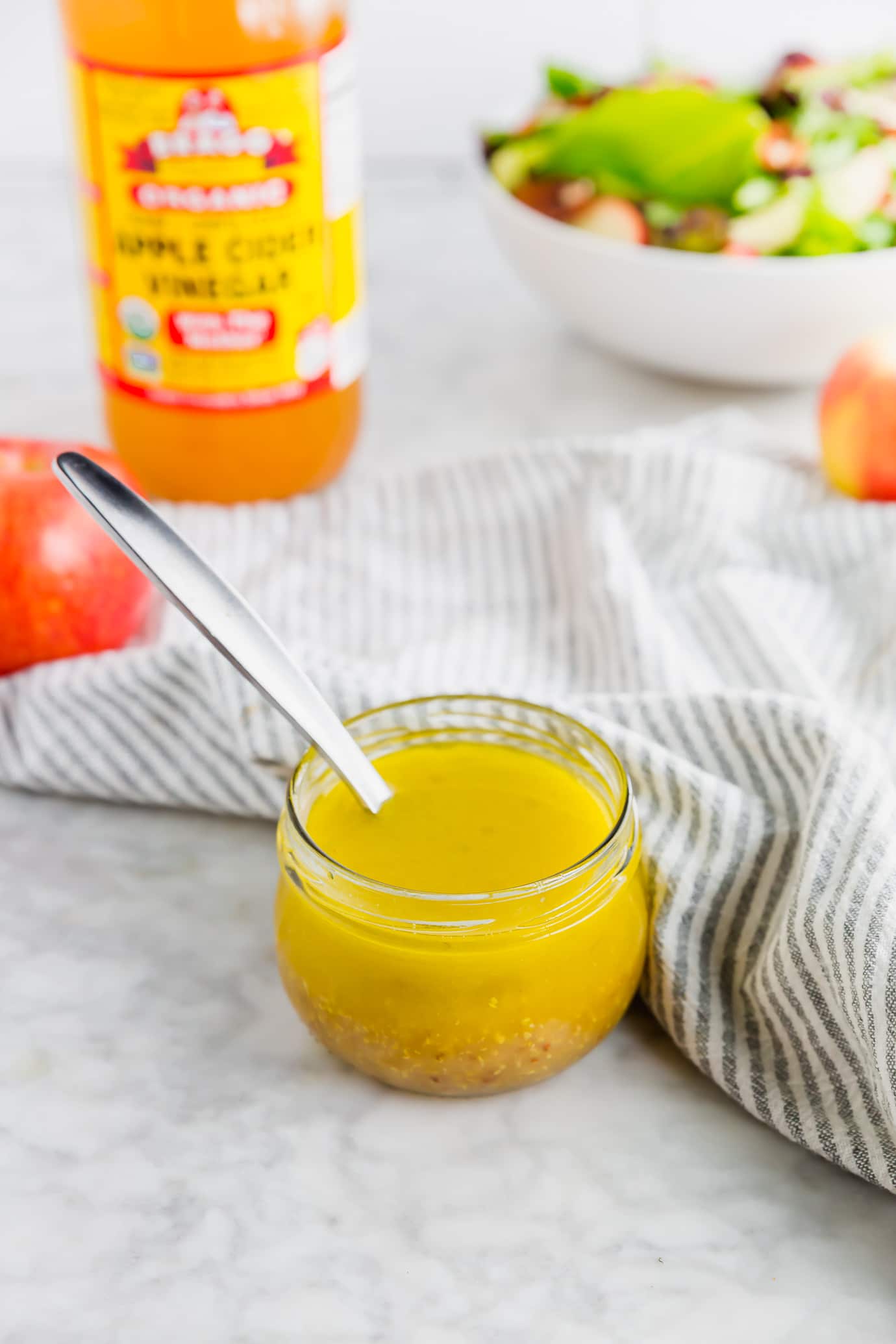 A photo of a jar of homemade apple vinaigrette with salad in the background.