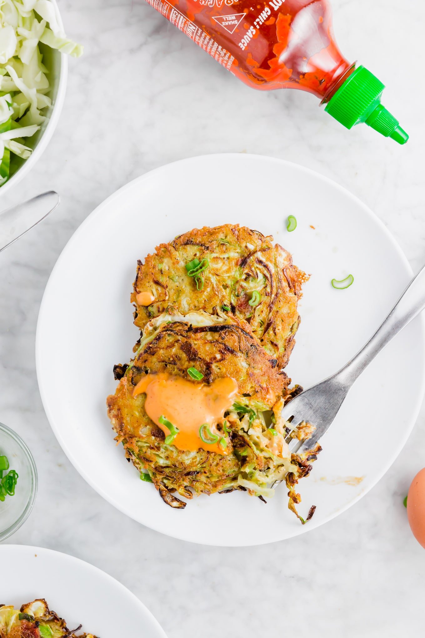 Cabbage bacon fritters topped with sriracha mayo and sliced green onions on a white plate.