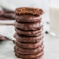 A stack of gluten-free thin mints on a marble table with the top cookie having a bite taken out of it.