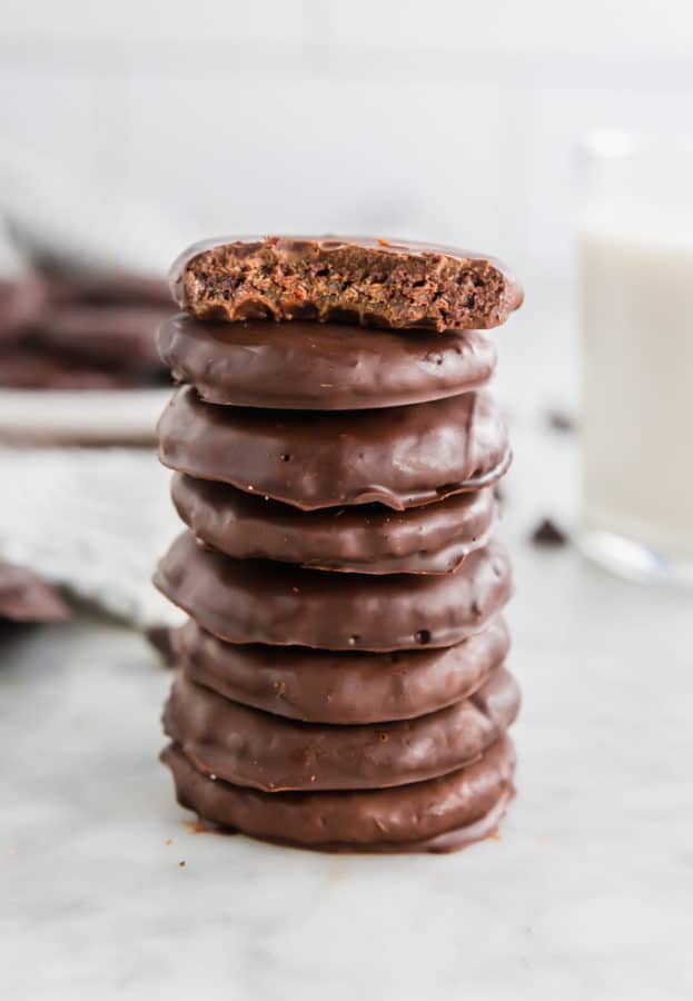 A stack of gluten-free thin mints on a marble table with the top cookie having a bite taken out of it. 
