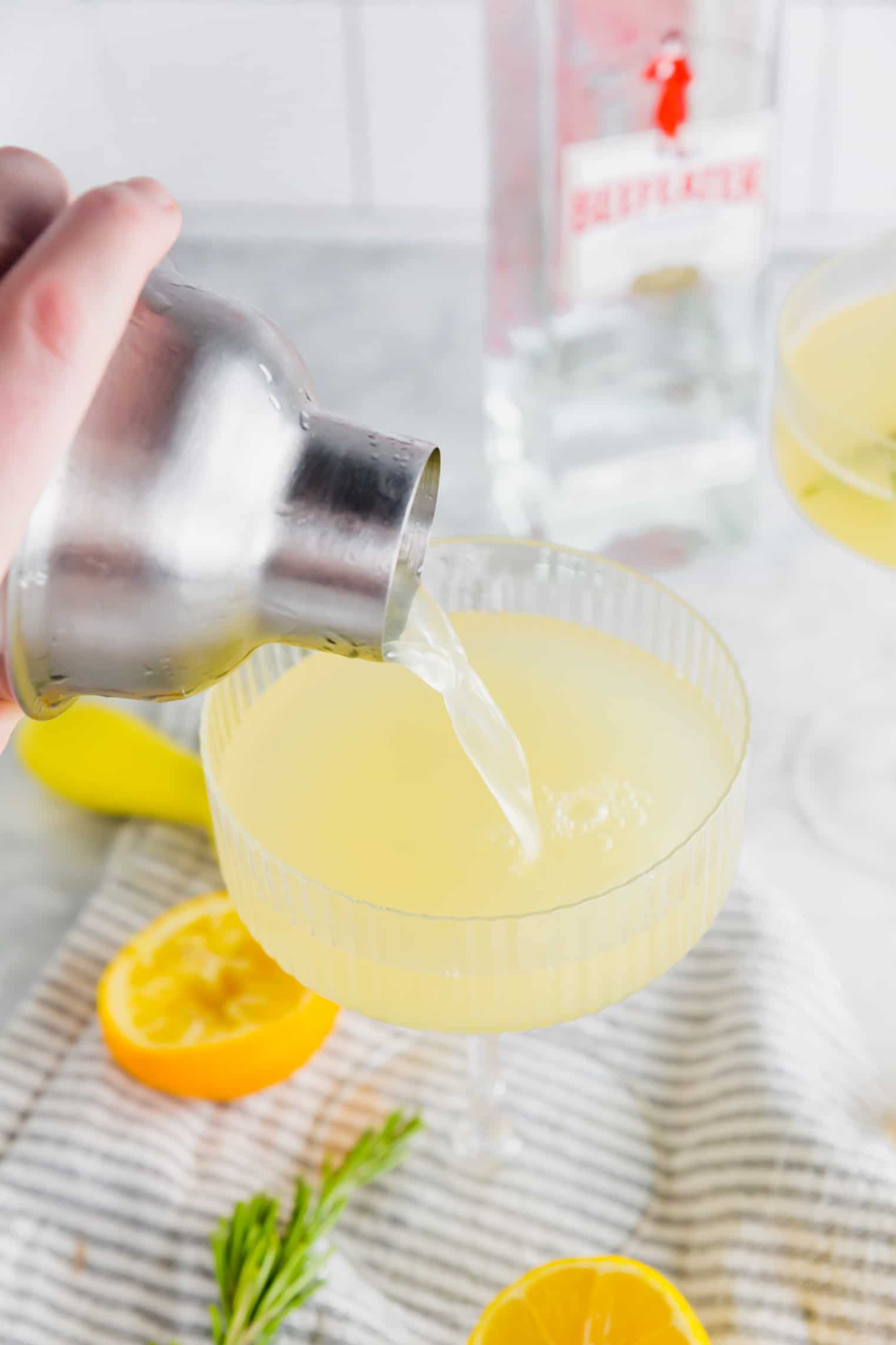 A cocktail shaker pouring meyer lemon gin cocktail into a coupe glass.